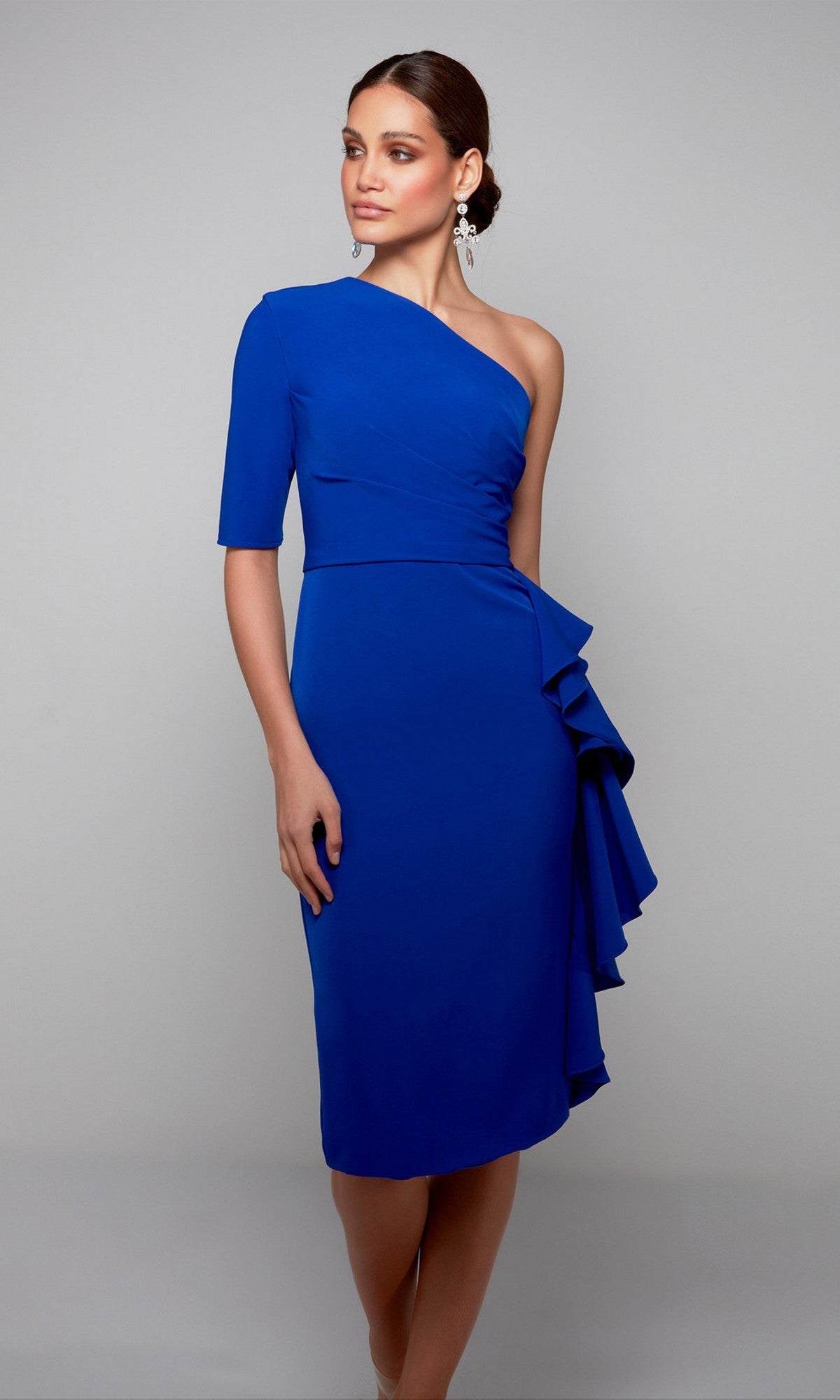 A woman poses against a plain grey background in the Alyce 70006 Knee Length Semi-Formal Dress, featuring a cobalt hue, one-shoulder design, and side ruffle detail.